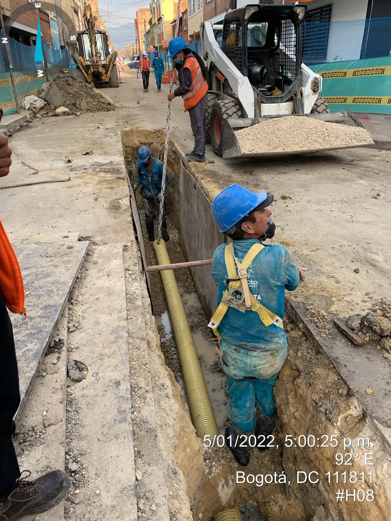 Personal asegurado con arnés instalando tubería de alcantarillado en zanja